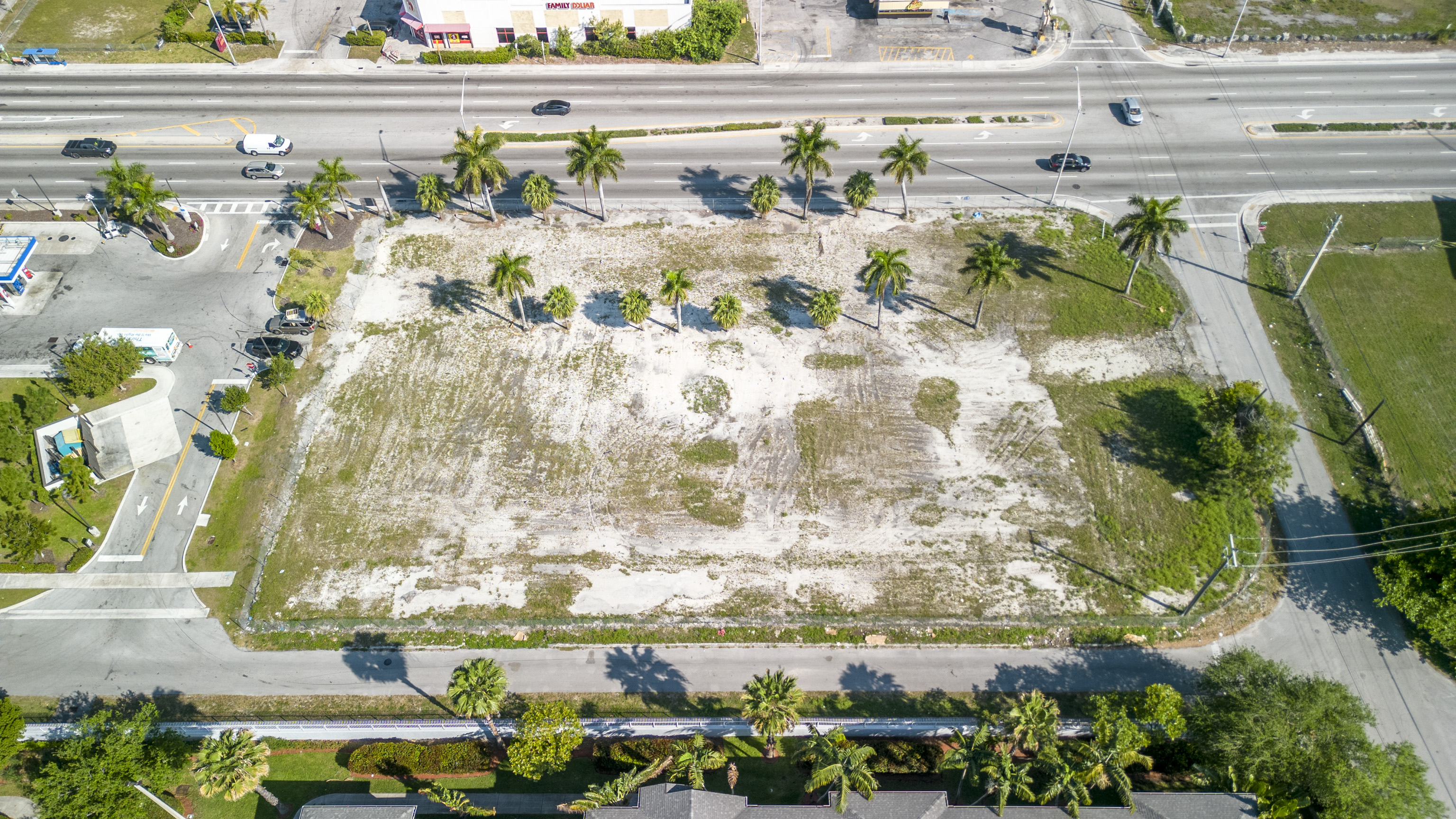 Aerial view of a vacant lot with palm trees and a road running along its edge.