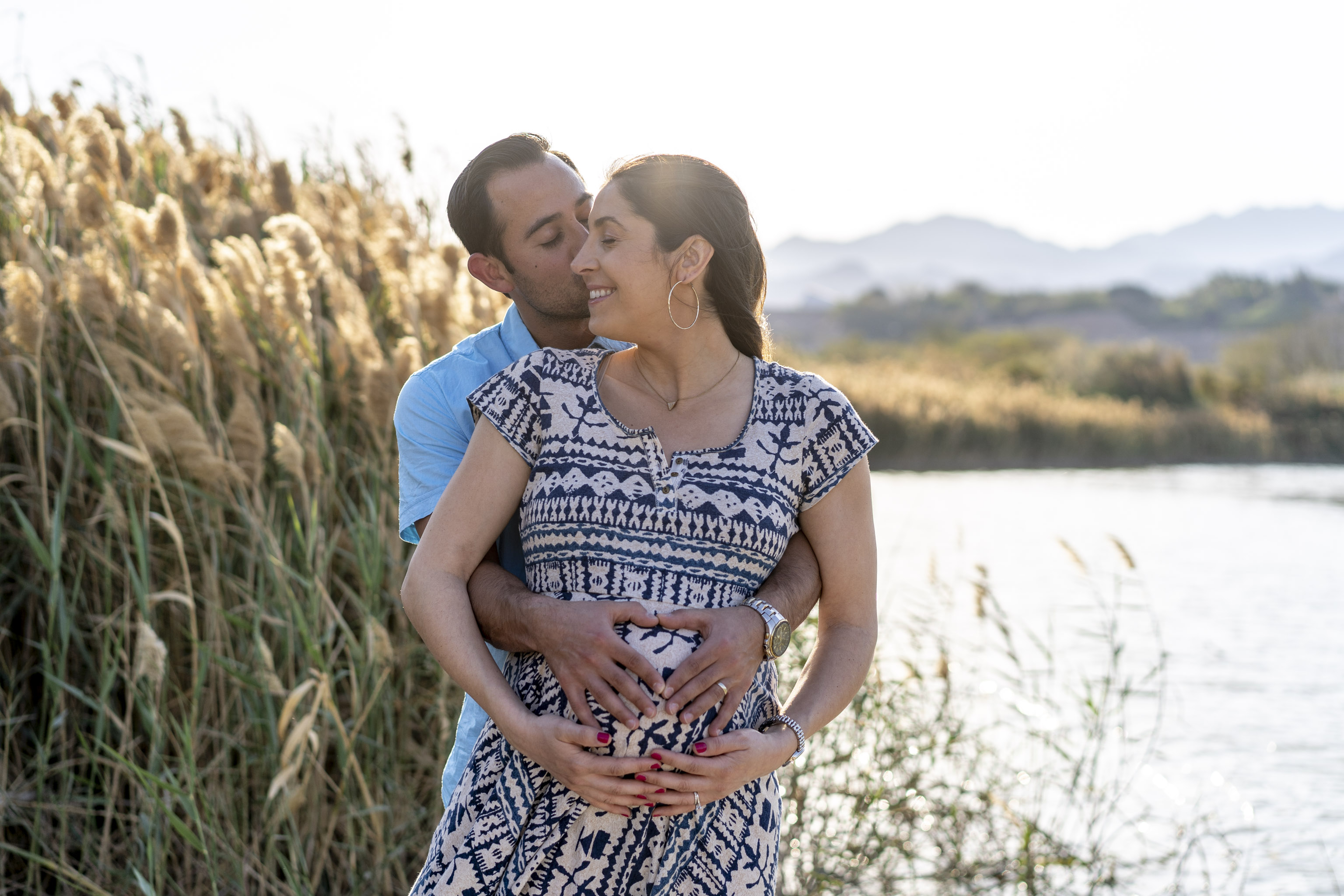 A man and woman stand together, embracing, with their hands on the woman's pregnant b