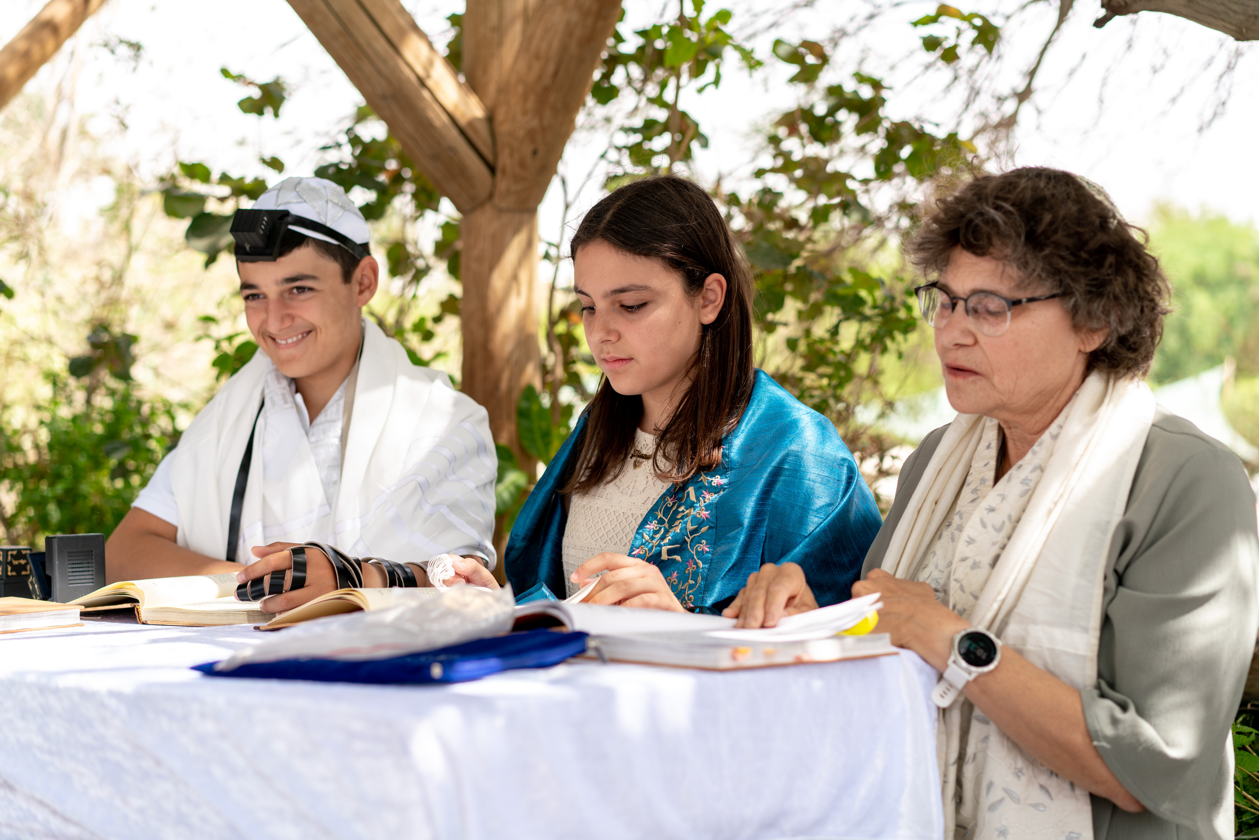 A young girl and boy sitting at a table, surrounded by books and papers, with a woman standing beside them.